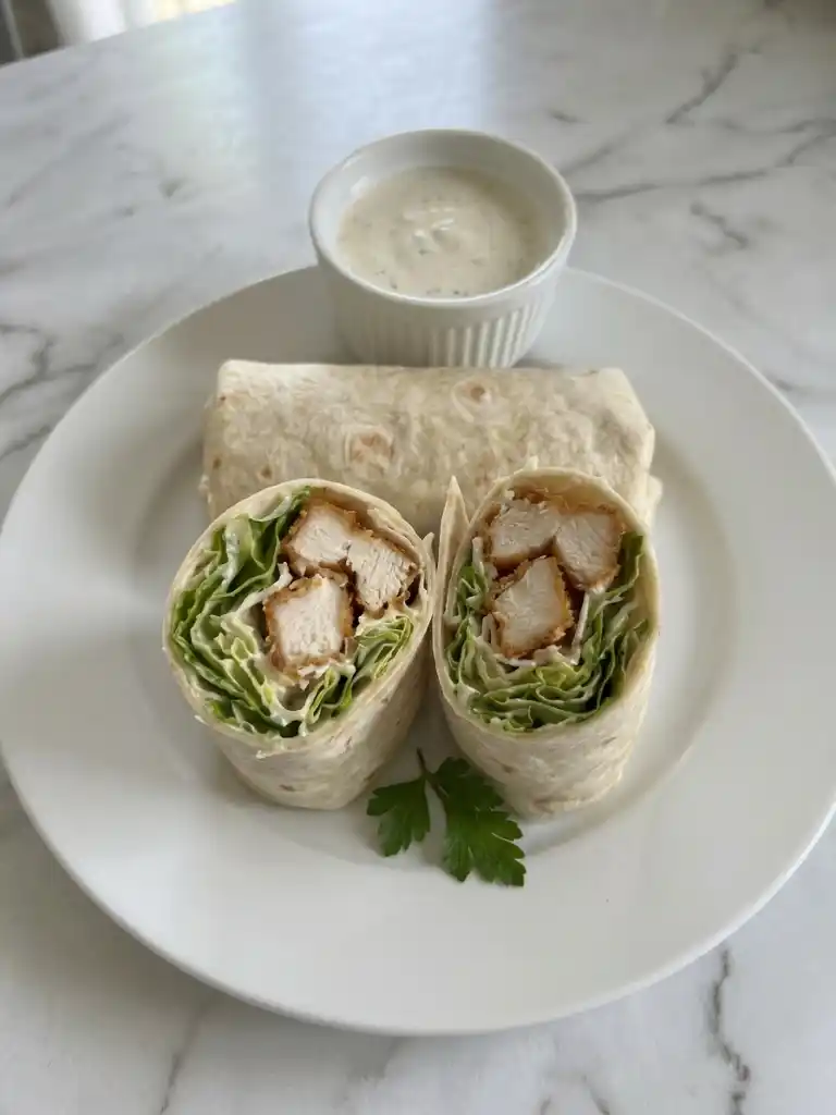 Chicken Caesar Wraps sliced open with crispy chicken, romaine, and Caesar dressing on a white plate