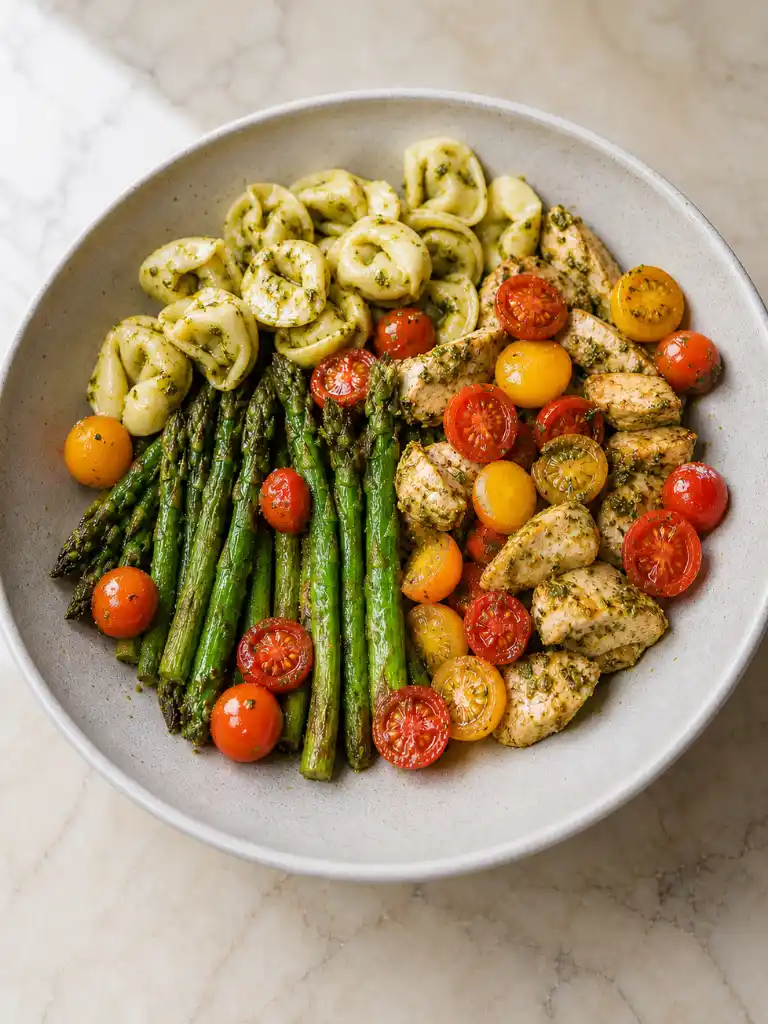 Pesto Chicken Tortellini and Veggies with roasted asparagus and cherry tomatoes in a bowl