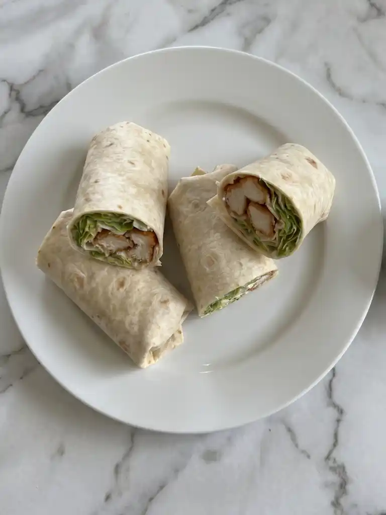 Chicken Caesar Wraps cut in halves with crispy chicken and romaine on a white plate